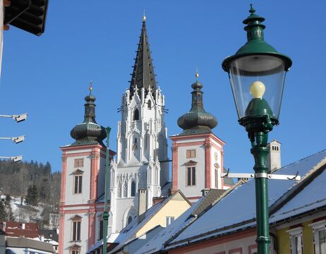 Barocke Kirchtürme mit hoher Spitze und schneebedeckten Dächern unter einem klaren blauen Himmel.