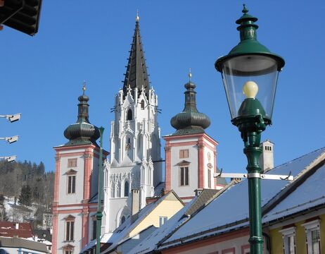 Barocke Kirchtürme mit hoher Spitze und schneebedeckten Dächern unter einem klaren blauen Himmel.