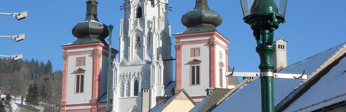 Barocke Kirchtürme mit hoher Spitze und schneebedeckten Dächern unter einem klaren blauen Himmel.