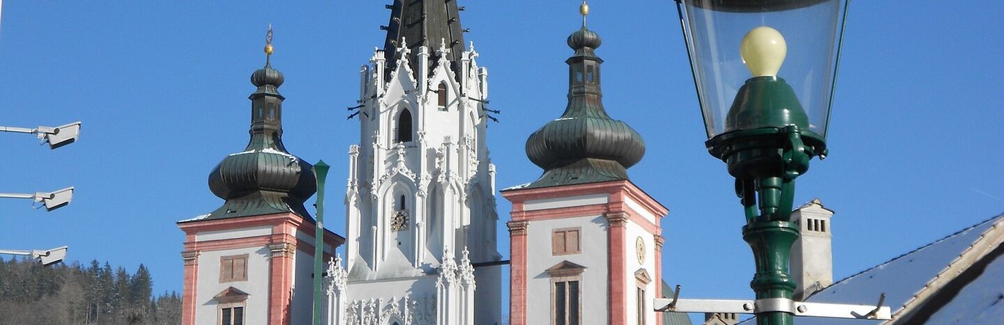Barocke Kirchtürme mit hoher Spitze und schneebedeckten Dächern unter einem klaren blauen Himmel.