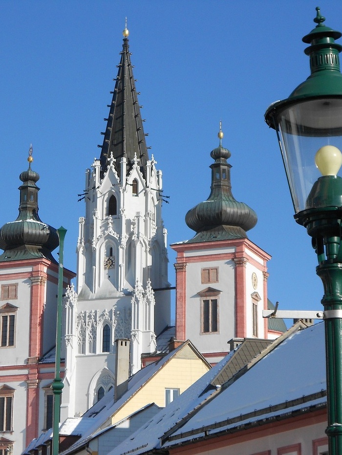 Barocke Kirchtürme mit hoher Spitze und schneebedeckten Dächern unter einem klaren blauen Himmel.