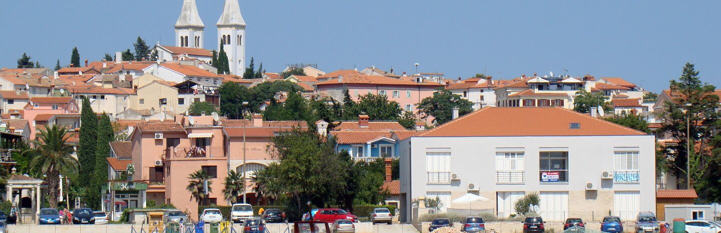 Kleine Boote auf ruhigem Wasser mit orangefarbenen Dächern und einem hohen weißen Kirchturm im Hintergrund.