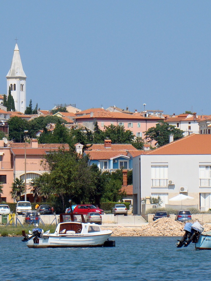 Kleine Boote auf ruhigem Wasser mit orangefarbenen Dächern und einem hohen weißen Kirchturm im Hintergrund.