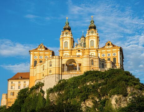 Gelbe Barockabtei mit Zwillingstürmen auf einem Hügel vor einem blauen Himmel mit einigen Wolken.