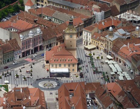 Luftaufnahme eines historischen Stadtplatzes mit Uhrenturm, roten Dächern und gemustertem Steinpflaster.