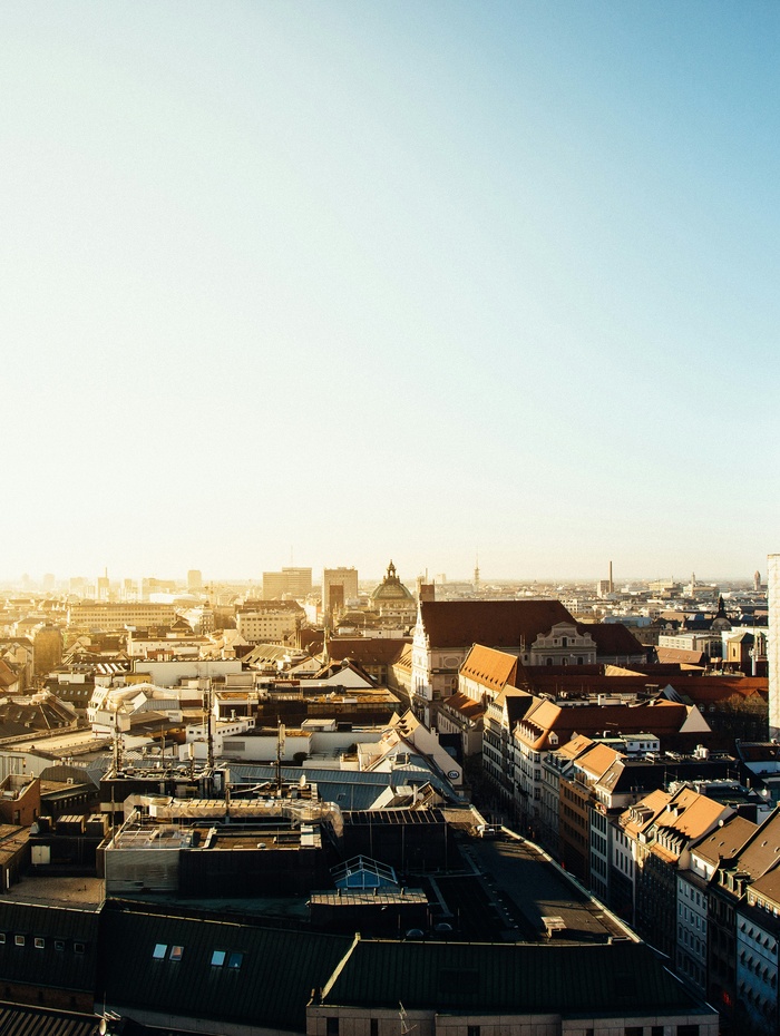 Ein Stadtbild bei Sonnenaufgang mit historischen Gebäuden und roten Dächern unter einem klaren blauen Himmel.