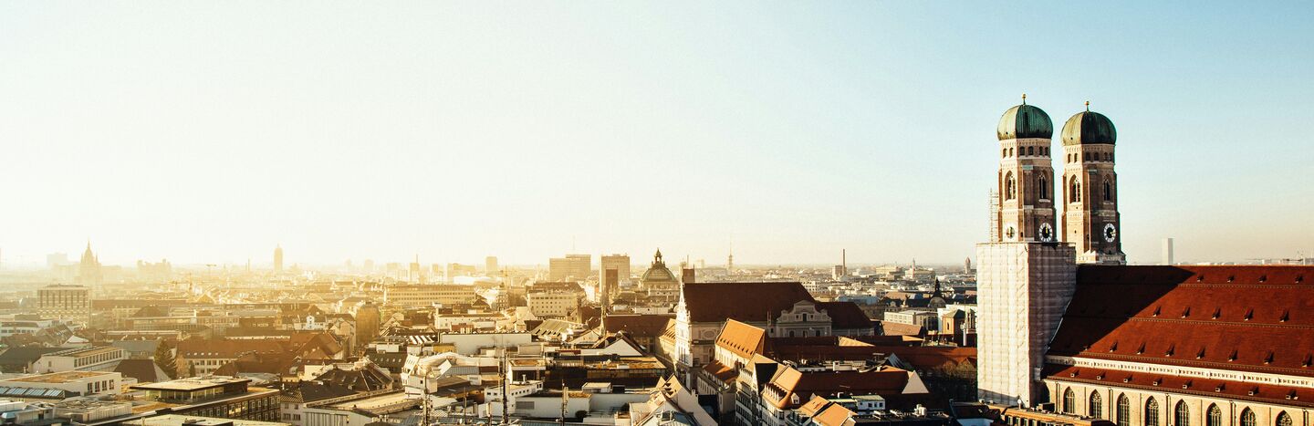Ein Stadtbild bei Sonnenaufgang mit historischen Gebäuden und roten Dächern unter einem klaren blauen Himmel.