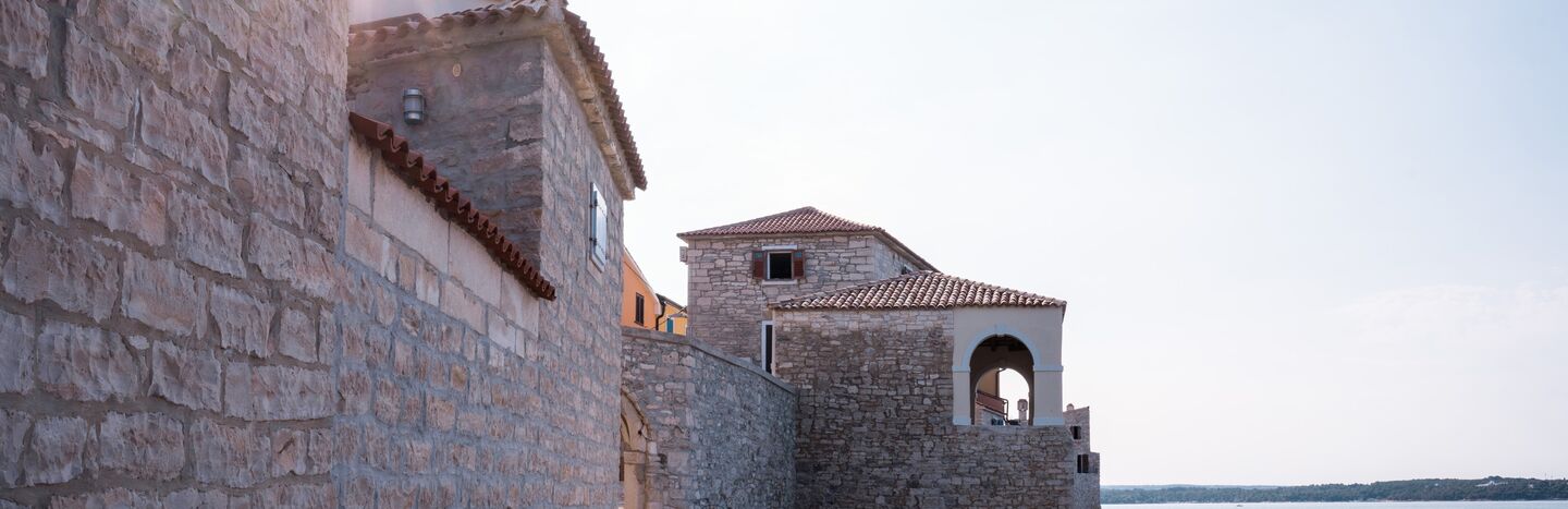 Steinpfade und Gebäude mit roten Ziegeldächern am Meer unter einem klaren Himmel.