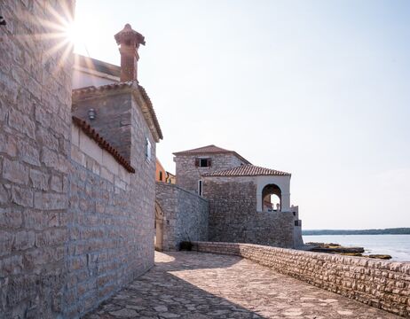 Steinpfade und Gebäude mit roten Ziegeldächern am Meer unter einem klaren Himmel.