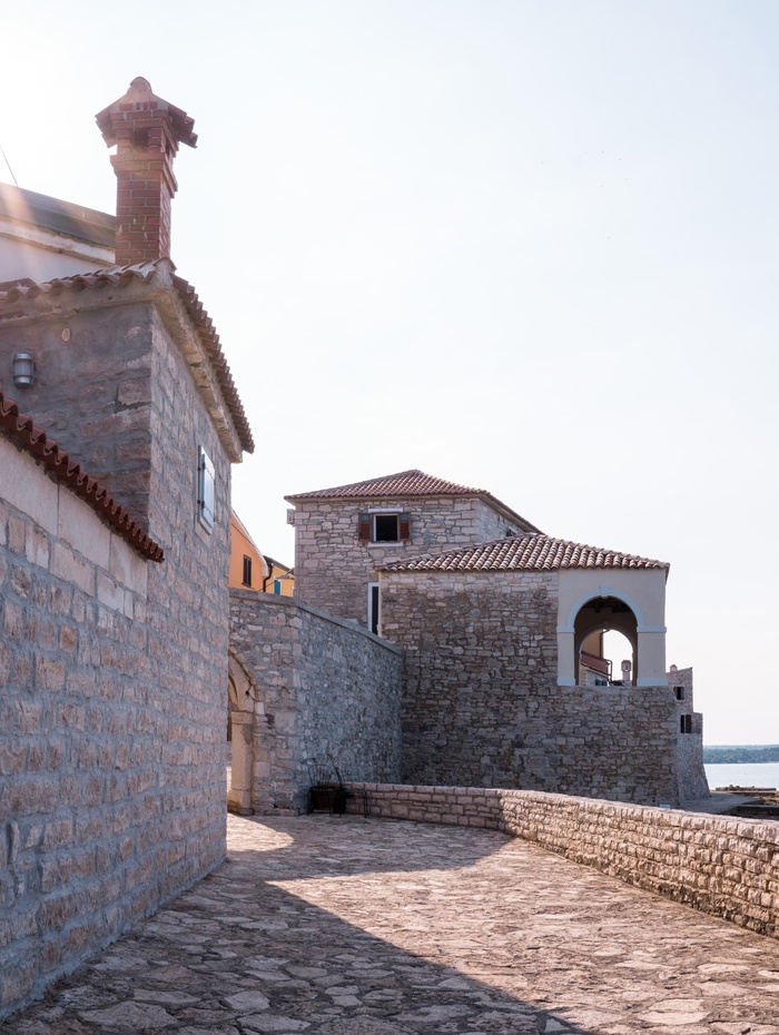 Steinpfade und Gebäude mit roten Ziegeldächern am Meer unter einem klaren Himmel.