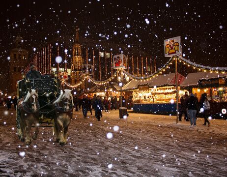 Schneefall auf einem festlichen Weihnachtsmarkt mit Lichtern, einer Pferdekutsche und Menschen, die herumlaufen.