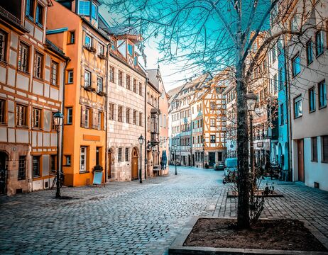 Eine Straße mit Kopfsteinpflaster, gesäumt von bunten, alten europäischen Gebäuden und kahlen Bäumen unter einem strahlend blauen Himmel.