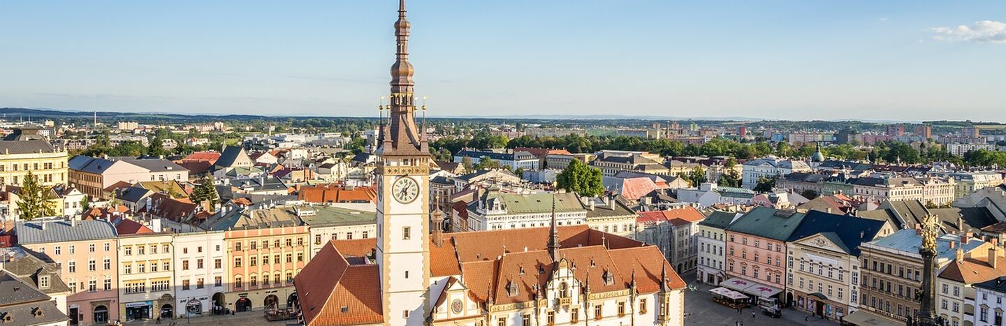 Luftaufnahme eines historischen Rathauses mit einem hohen Uhrenturm auf einem europäischen Stadtplatz.