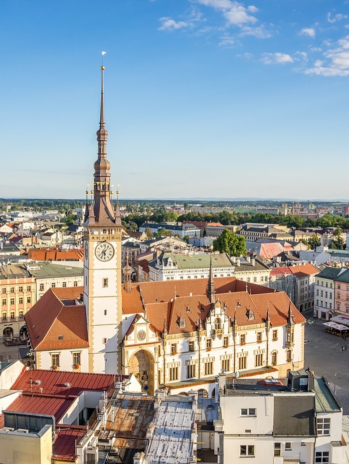 Luftaufnahme eines historischen Rathauses mit einem hohen Uhrenturm auf einem europäischen Stadtplatz.