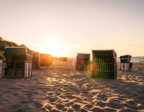 Sonnenuntergang über dem Sandstrand mit gestreiften Strandkörben, die den Weg zum Meer säumen.
