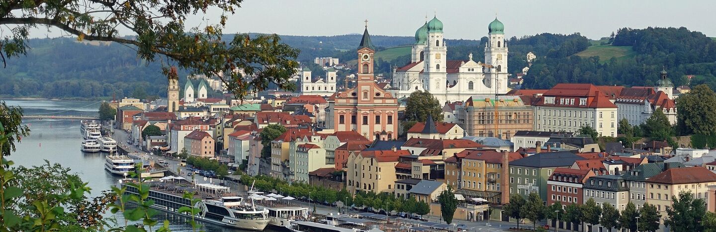 Eine europäische Stadt am Flussufer mit farbenfrohen Gebäuden, Kirchen und Booten, die entlang des Wassers ankern.