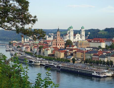 Eine europäische Stadt am Flussufer mit farbenfrohen Gebäuden, Kirchen und Booten, die entlang des Wassers ankern.