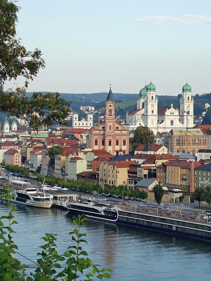 Eine europäische Stadt am Flussufer mit farbenfrohen Gebäuden, Kirchen und Booten, die entlang des Wassers ankern.