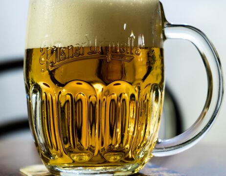 Ein Glaskrug mit goldenem Bier und einer dicken Schaumkrone steht auf einem Tisch.