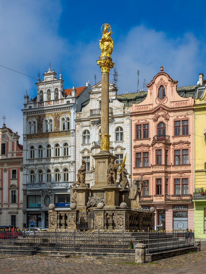 Eine barocke Mariensäule mit Statuen, umgeben von kunstvoll verzierten historischen Gebäuden auf einem Stadtplatz.