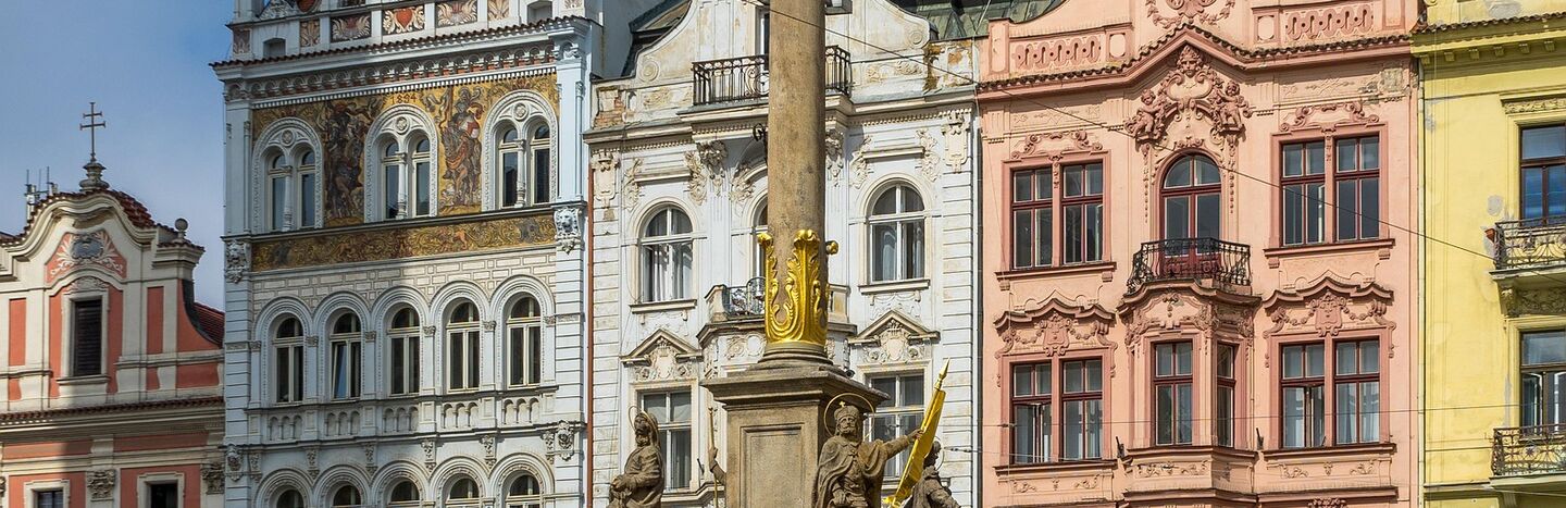 Eine barocke Mariensäule mit Statuen, umgeben von kunstvoll verzierten historischen Gebäuden auf einem Stadtplatz.