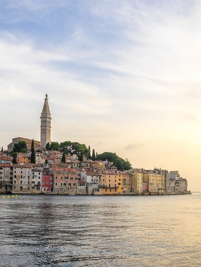 Ein weißes Kloster am See mit einem hohen Zwiebelturm vor dem Hintergrund von bewaldeten Bergen und blauem Himmel.