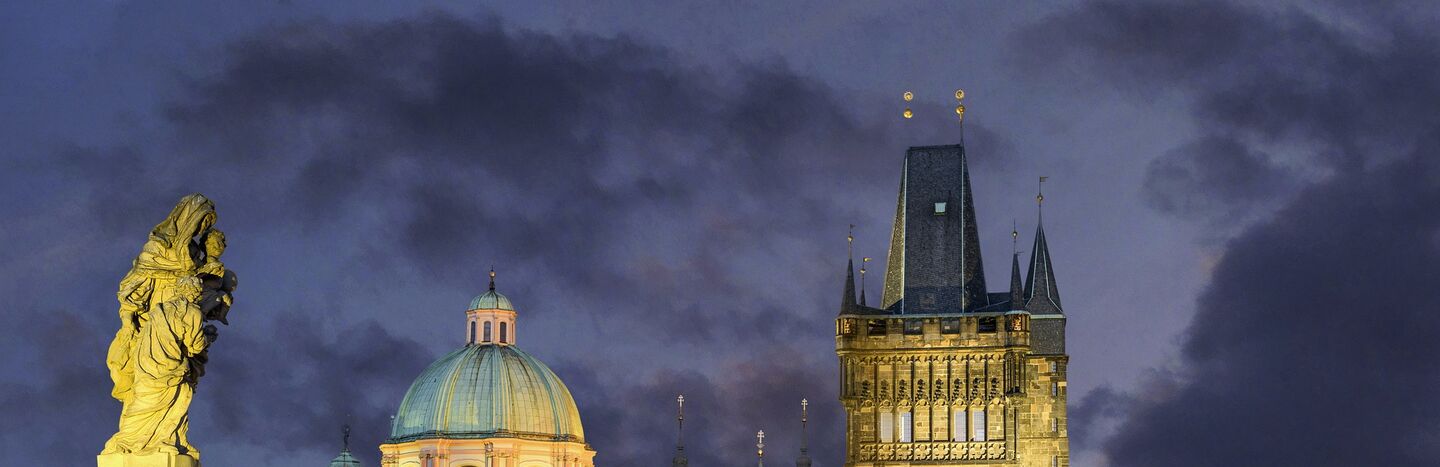 Die Karlsbrücke in Prag in der Abenddämmerung, mit historischen Gebäuden und Straßenlaternen, die bei bewölktem Himmel beleuchtet sind.