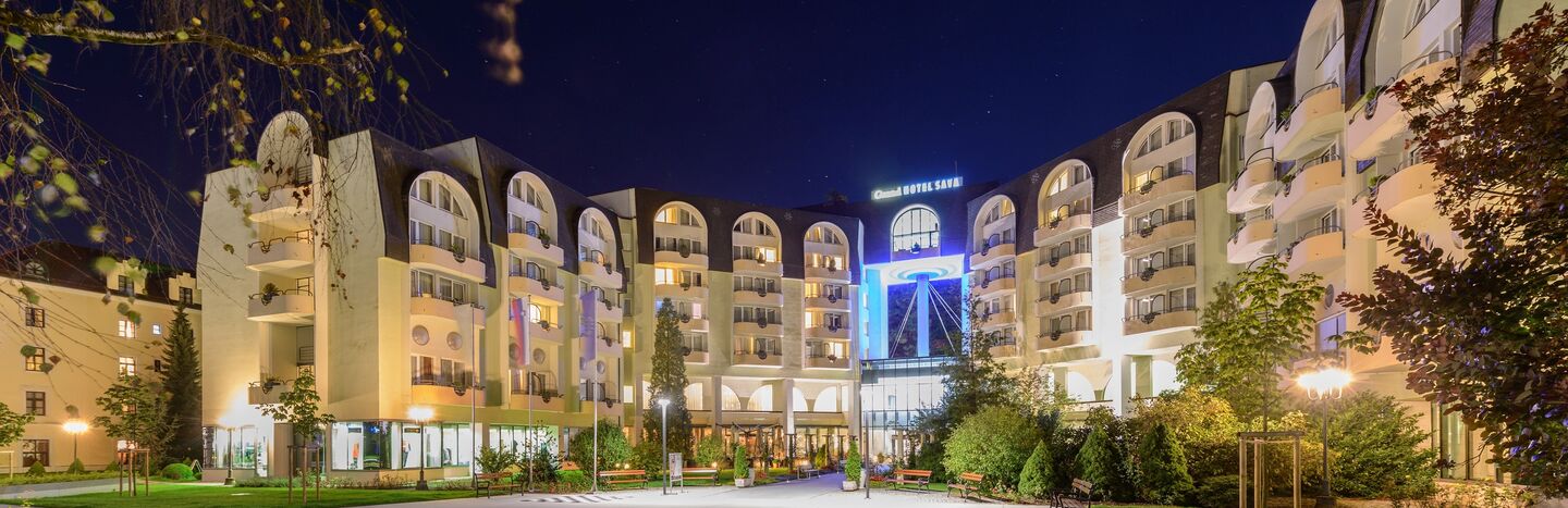 Ein nachts hell erleuchtetes Hotel mit gewölbten Balkonen und einem geräumigen Vorhof.