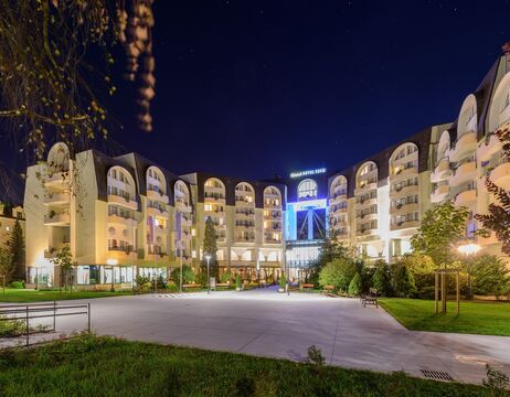 Ein nachts hell erleuchtetes Hotel mit gewölbten Balkonen und einem geräumigen Vorhof.