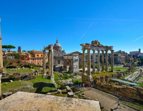 Antike römische Ruinen mit hohen Säulen und einem Kuppelbau im Hintergrund unter einem klaren blauen Himmel.