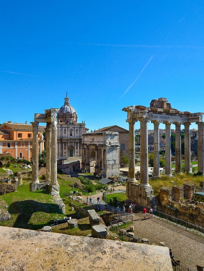 Antike römische Ruinen mit hohen Säulen und einem Kuppelbau im Hintergrund unter einem klaren blauen Himmel.