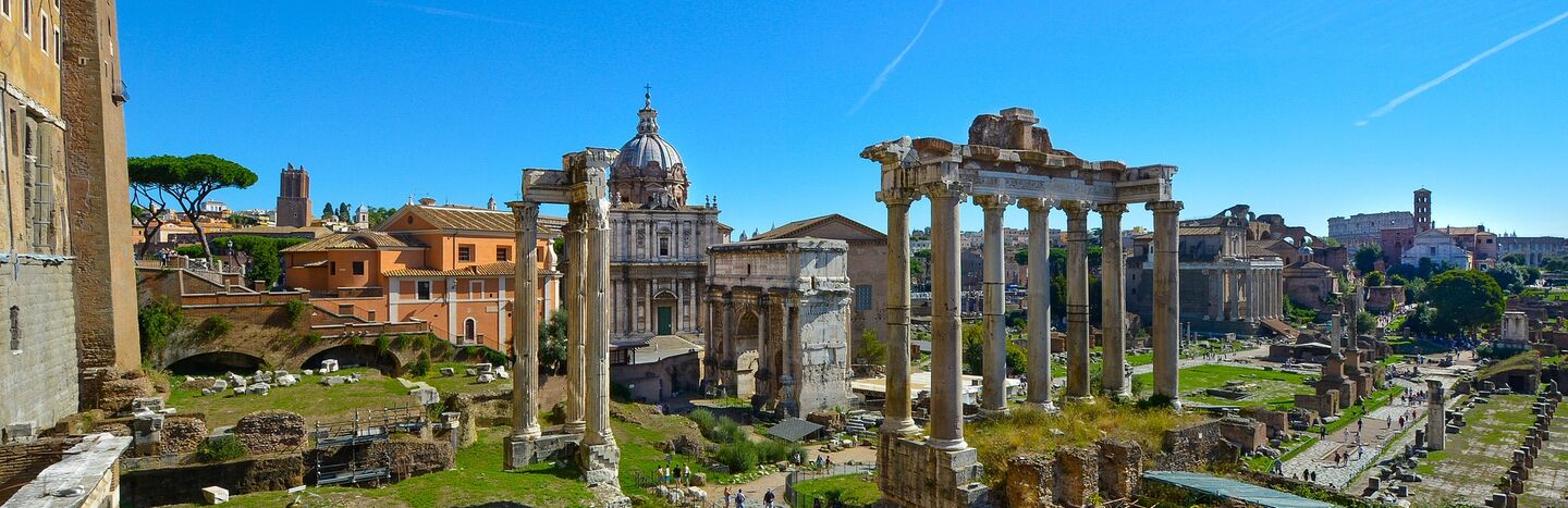 Antike römische Ruinen mit hohen Säulen und einem Kuppelbau im Hintergrund unter einem klaren blauen Himmel.