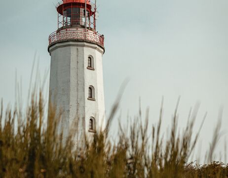 Ein weißer Leuchtturm mit roter Spitze erhebt sich hinter verschwommenem grünem Gras unter einem klaren Himmel.