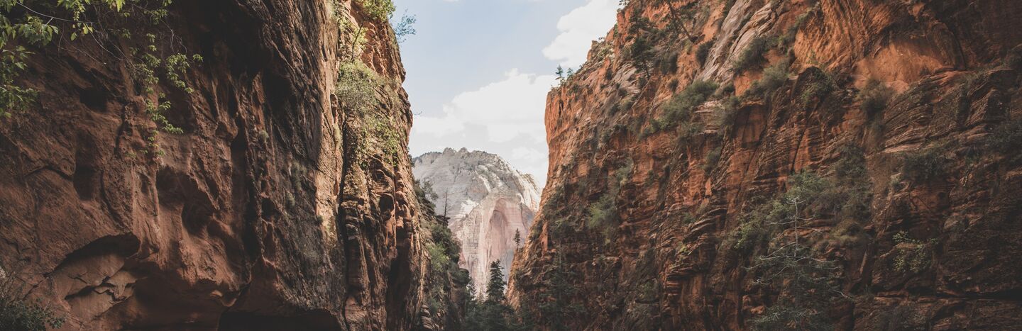 Enger Canyon mit hohen roten Felswänden und Kiefern, unter einem teilweise bewölkten Himmel.