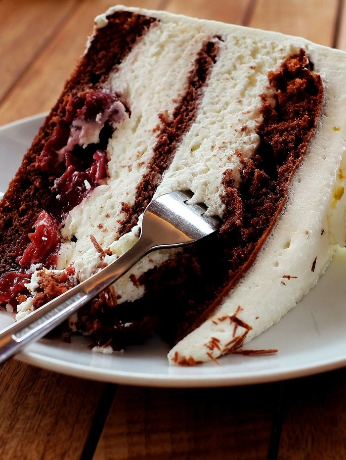 Eine Gabel liegt auf einem Teller, auf dem ein Stück Schokoladen-Sahne-Torte mit Kirschen liegt.