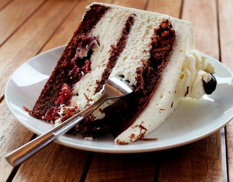 Eine Gabel liegt auf einem Teller, auf dem ein Stück Schokoladen-Sahne-Torte mit Kirschen liegt.