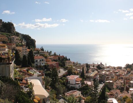 Ein Dorf am Hang mit mediterranen Häusern und Blick auf das Meer unter einem klaren, sonnigen Himmel.
