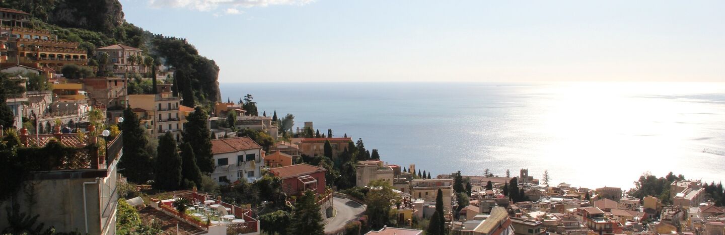 Ein Dorf am Hang mit mediterranen Häusern und Blick auf das Meer unter einem klaren, sonnigen Himmel.