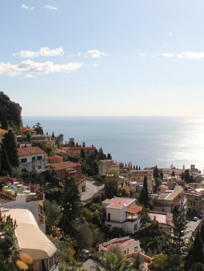 Ein Dorf am Hang mit mediterranen Häusern und Blick auf das Meer unter einem klaren, sonnigen Himmel.