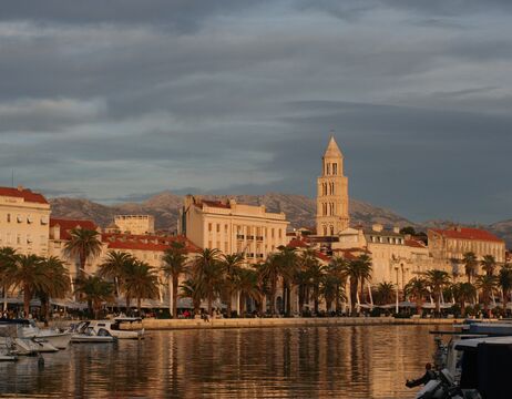 Blick aufs Wasser in Split, Kroatien, mit Palmen, historischen Gebäuden und einem Glockenturm bei Sonnenuntergang.