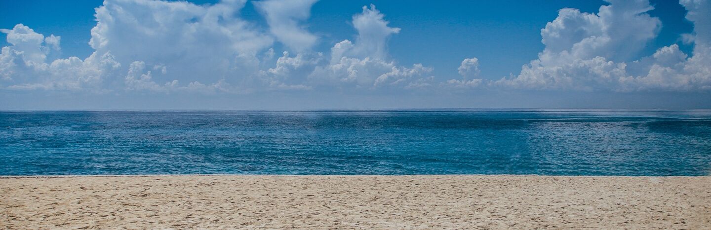 Sandstrand mit ruhigem blauen Meer unter einem klaren Himmel mit vereinzelten Wolken.