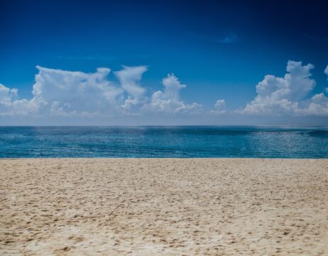 Sandstrand mit ruhigem blauen Meer unter einem klaren Himmel mit vereinzelten Wolken.