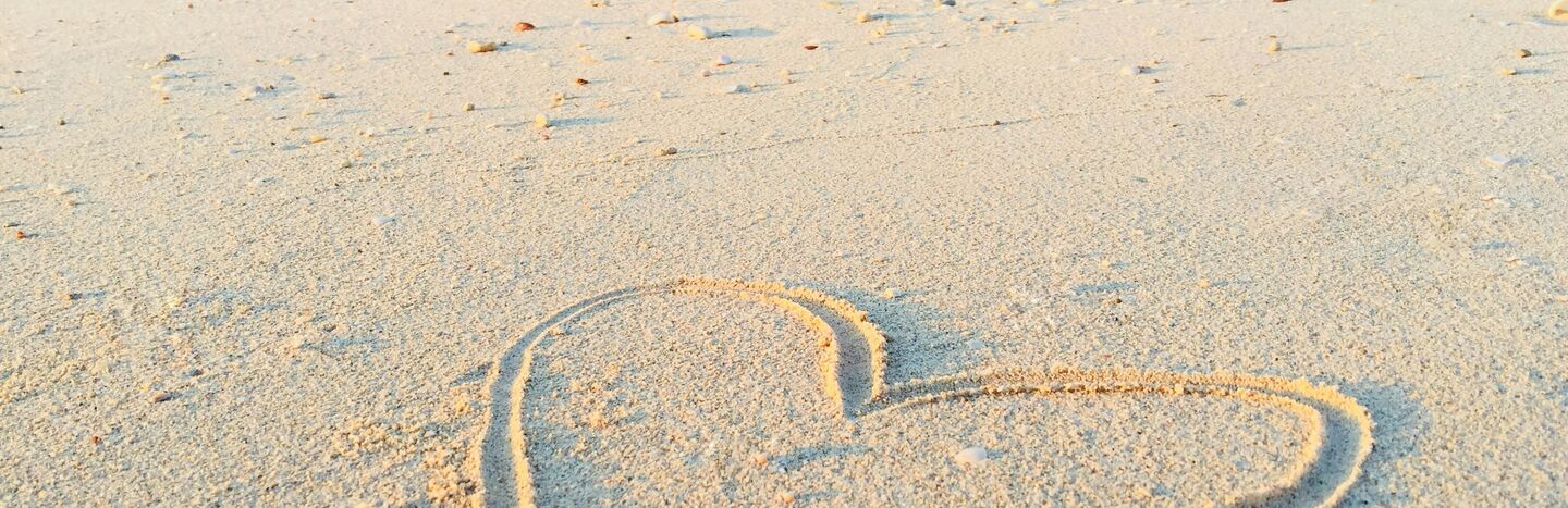 Eine Person mit Hut sitzt auf einer felsigen Klippe und blickt unter einem blauen Himmel mit Wolkenfetzen auf den Ozean hinaus.