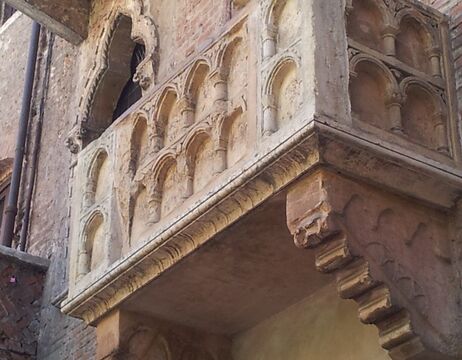 Nahaufnahme eines steinernen Balkons mit verschnörkelten Bögen an einem alten Backsteingebäude.