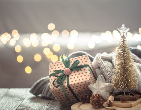 Polka-Dot-Geschenkbox mit grünem Band, kuscheliger Decke, Stern-Ornament und warmen Lichterketten im Hintergrund.