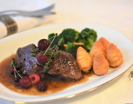 Ein Tellergericht mit Rindfleisch, Soße, Beeren, Brokkoli und drei Herzoginkartoffeln auf einem weißen Teller.
