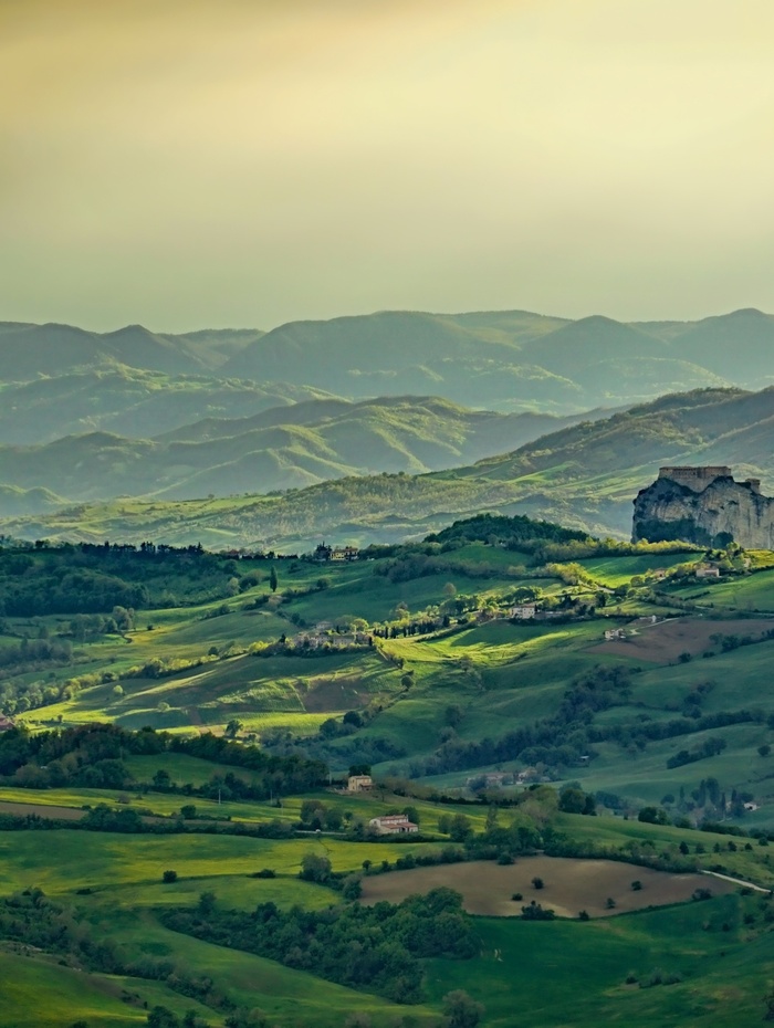 Eine malerische Aussicht auf sanfte grüne Hügel und Berge unter einem bewölkten Himmel bei Sonnenuntergang.