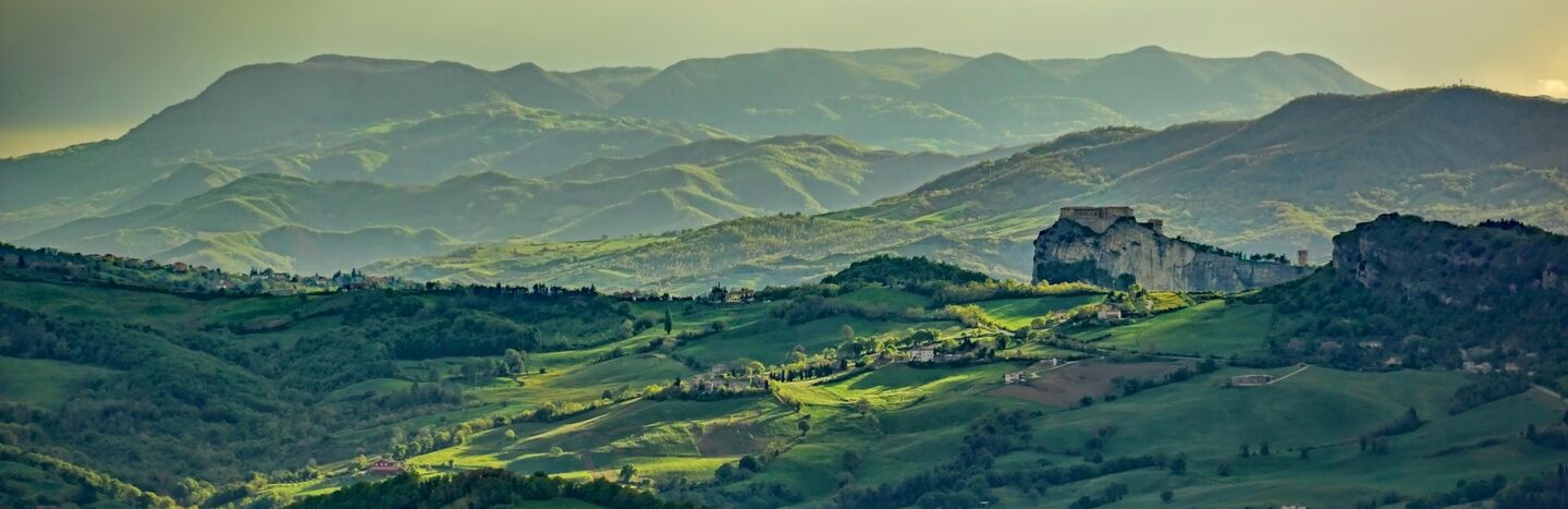 Eine malerische Aussicht auf sanfte grüne Hügel und Berge unter einem bewölkten Himmel bei Sonnenuntergang.