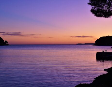 Lila und orangefarbener Sonnenuntergang über einem ruhigen Meer mit einer entfernten dunklen Landmasse am Horizont.