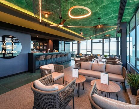 Moderne Rooftop-Bar mit stilvollen Sitzgelegenheiten, grüner Decke und großen Fenstern mit Blick auf die Skyline der Stadt.